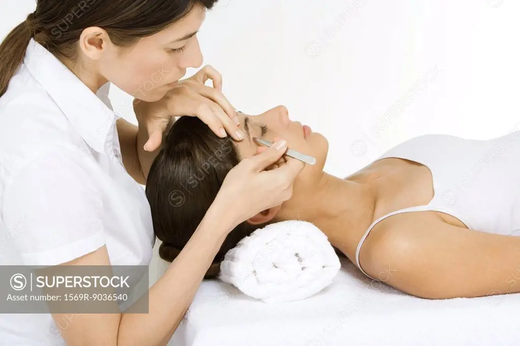 Woman lying on her back having her eyebrows plucked by a beautician