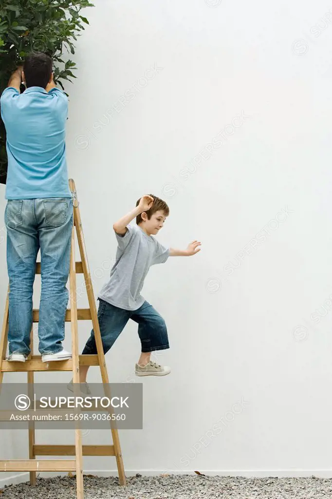 Father and son standing on ladder, boy leaping off