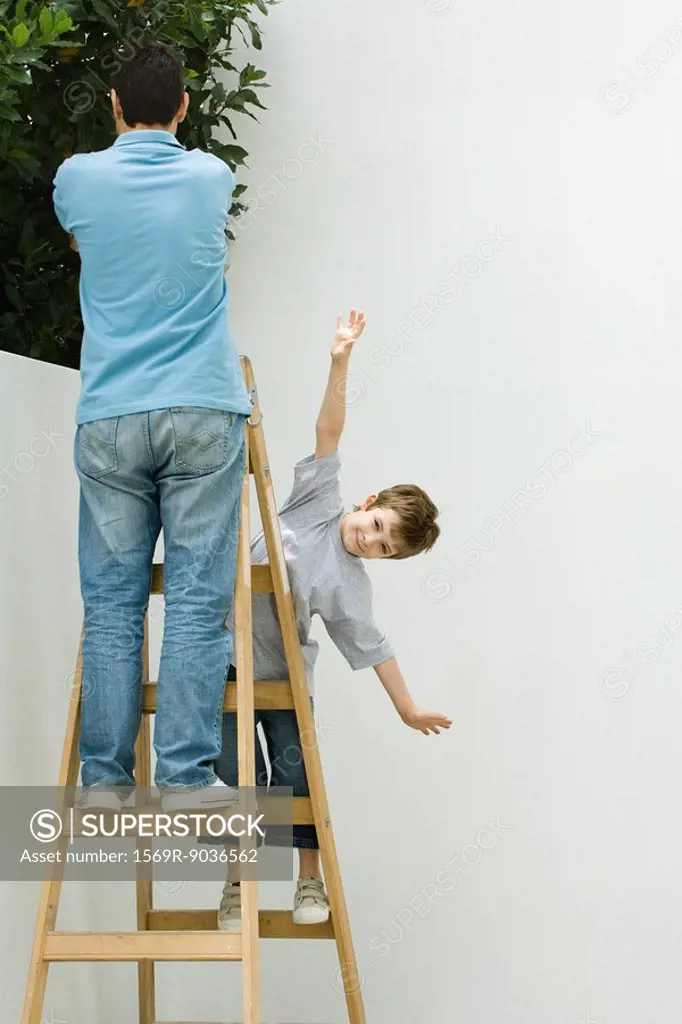 Father and son standing on ladder, boy pretending to be a plane