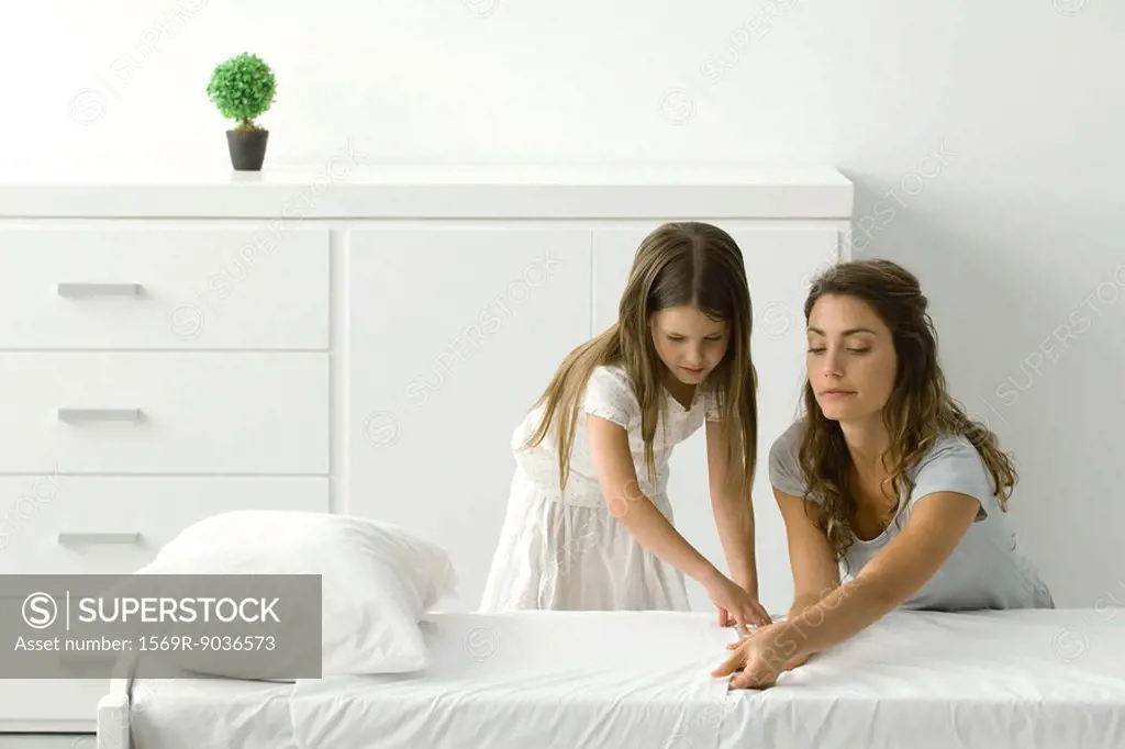 Mother and daughter making bed together