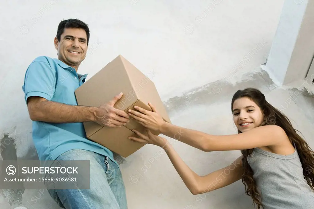 Father and daughter moving cardboard box together, low angle view