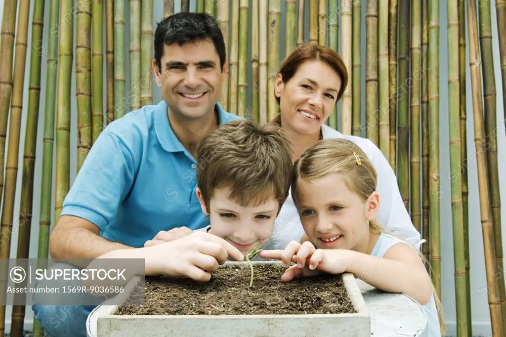 Family together, parents smiling at camera, children touching potted seedling