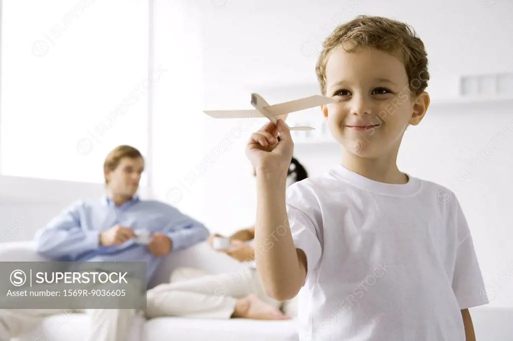 Boy playing with toy airplane, parents sitting on couch in background