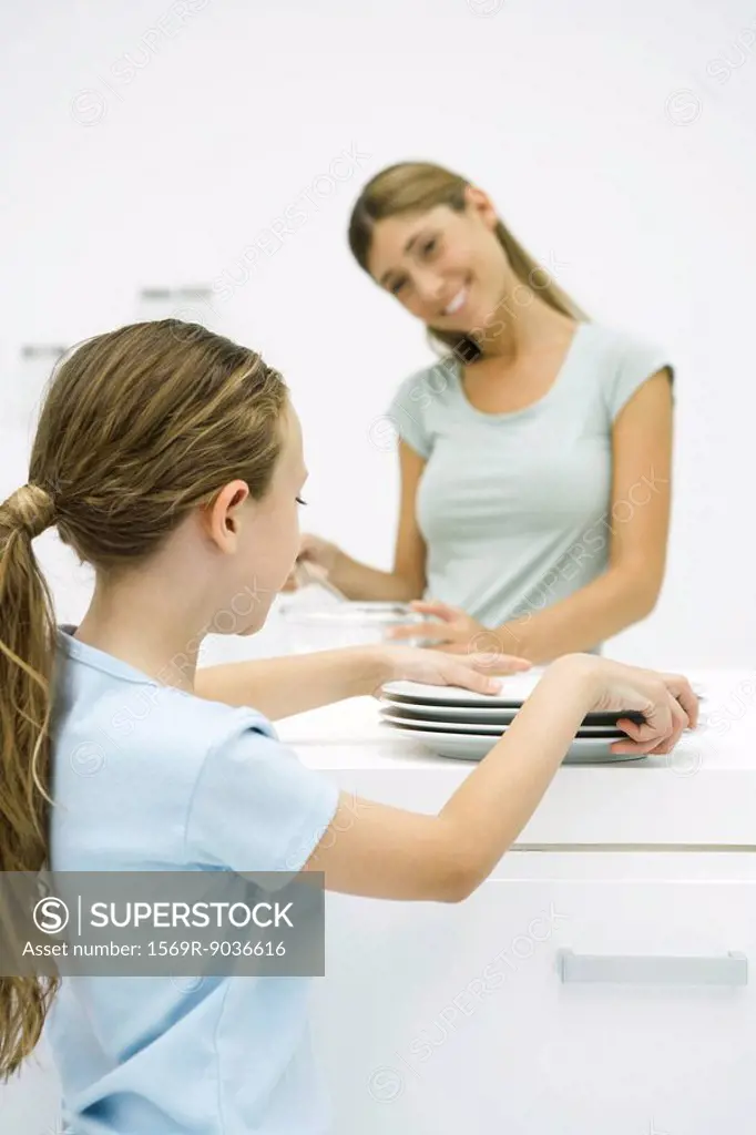 Girl picking up plates, mother smiling at her