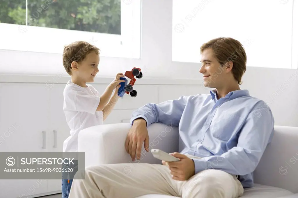 Little boy showing his father a toy truck, man holding remote control