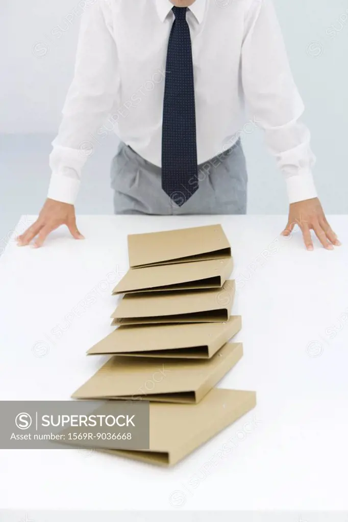 Binders lying on table after a chain reaction of being pushed over, cropped view of businessman