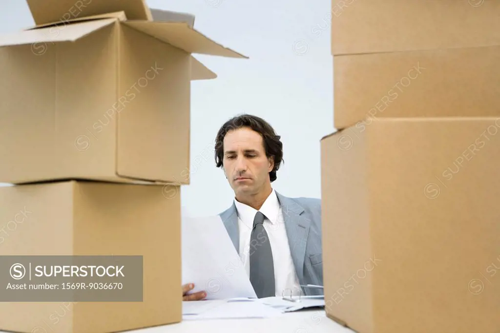Professional man reading document, cardboard boxes piled up on both sides