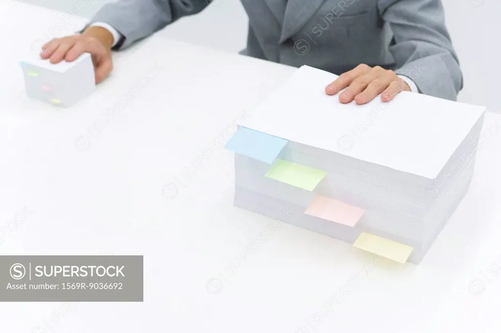 Stacks of paper with adhesive notes dividing them, man putting one hand on each stack