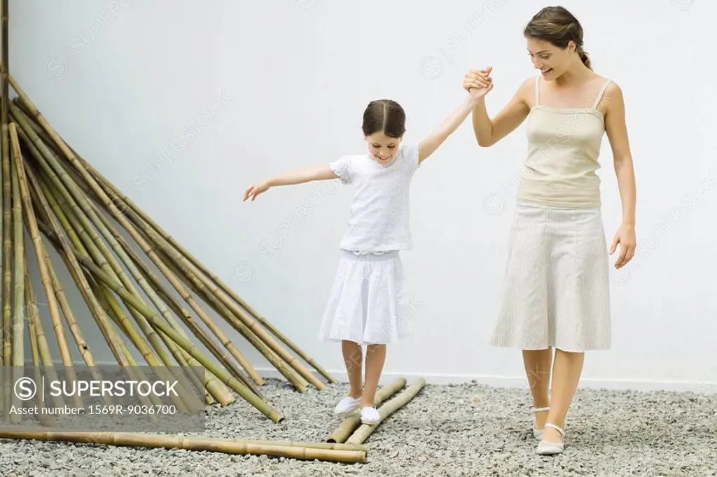 Girl balancing on bamboo, mother helping her by holding her hand