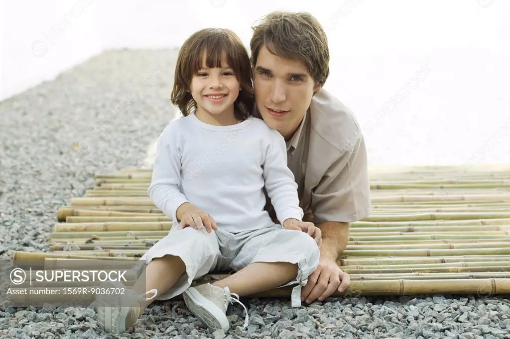 Young man and son on bamboo together, both smiling at camera