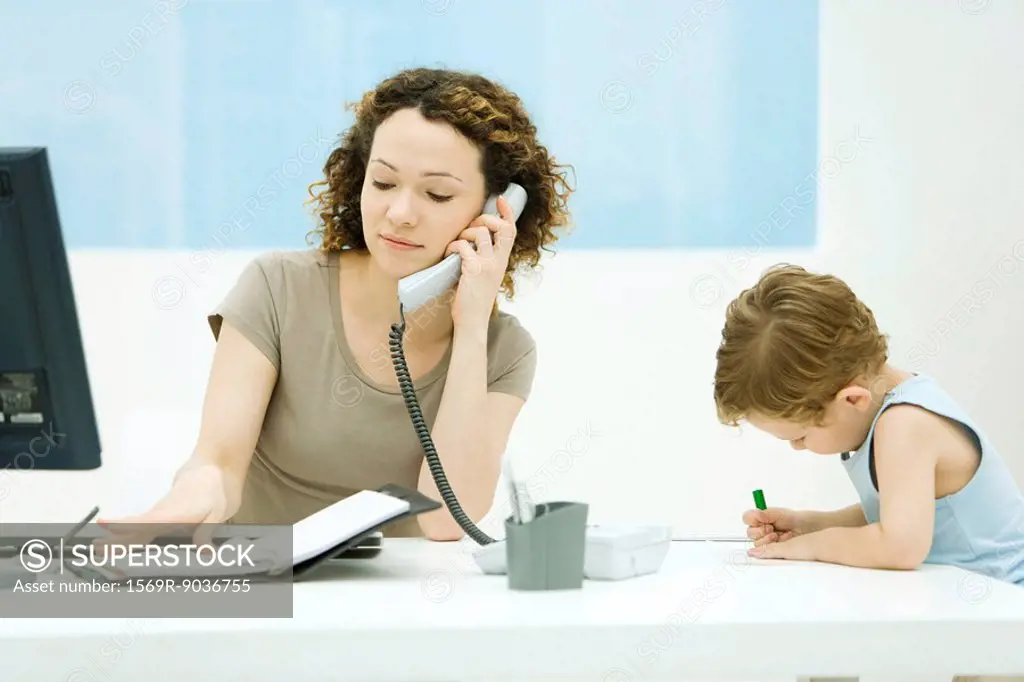 Woman using phone and looking at agenda, young son sitting beside her, coloring