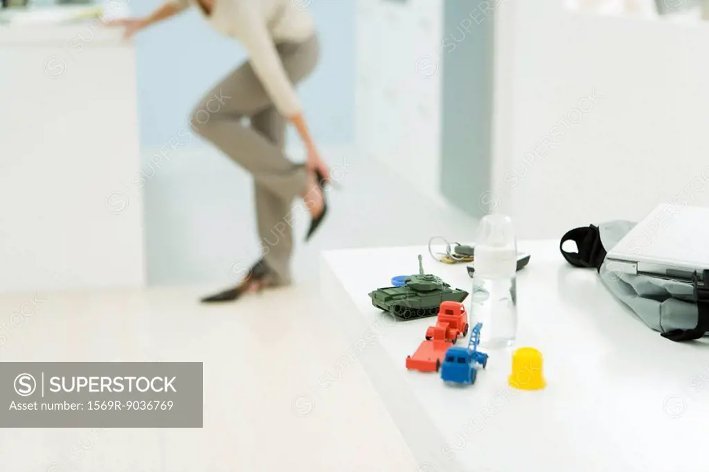 Professional woman getting dressed, focus on baby bottle and toys in foreground