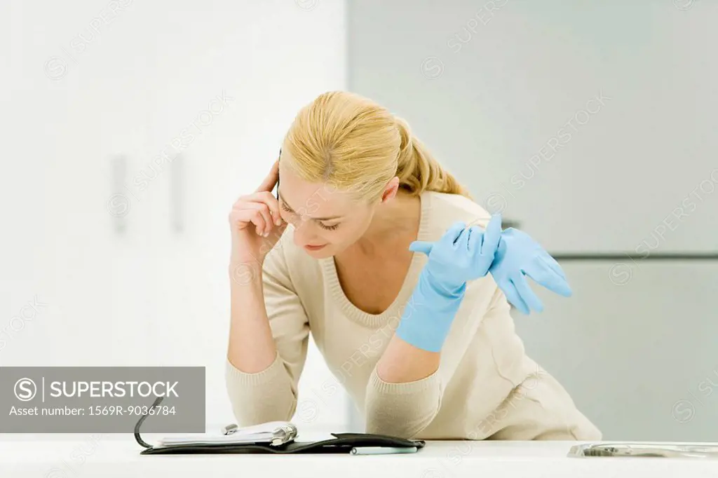 Young woman wearing rubber gloves, using cell phone and looking down at agenda