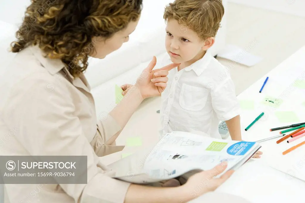 Mother holding magazine, looking at son, holding his chin