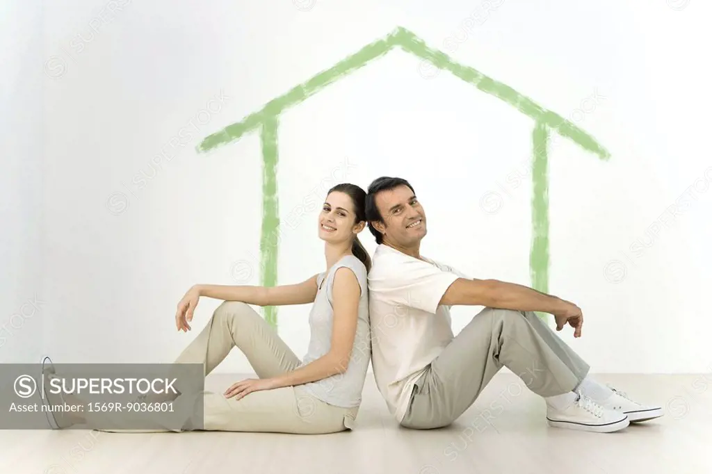 Couple sitting back to back in front of an outline of a house painted on wall