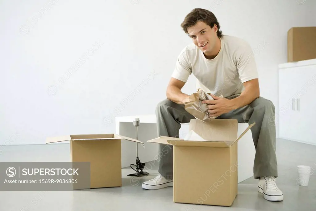 Man unpacking boxes, sitting on bench, smiling at camera