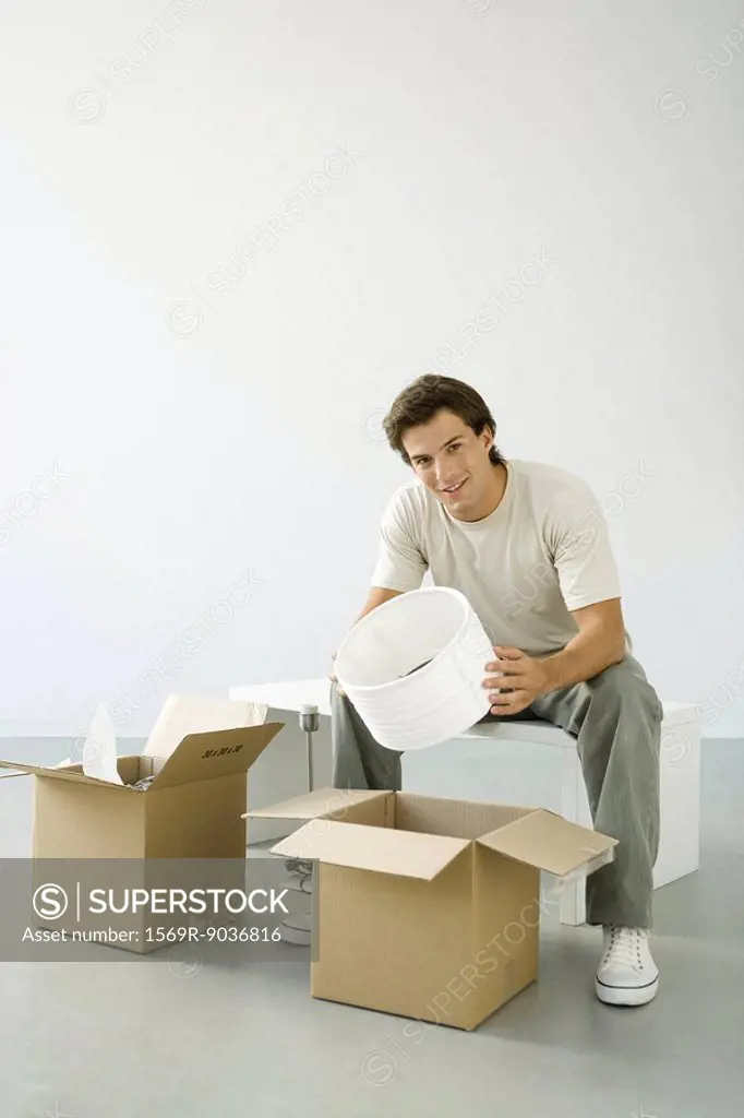 Man unpacking boxes, holding lampshade, smiling at camera