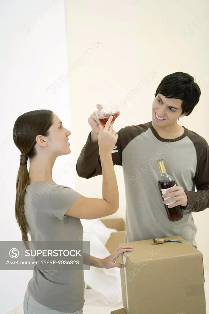 Couple clinking glasses of red wine, cardboard boxes nearby