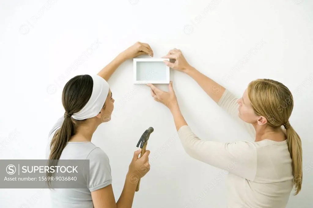 Mother and daughter attaching picture frame to wall