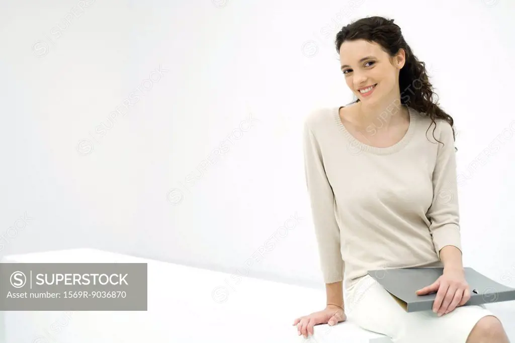 Young professional woman holding binder, smiling at camera