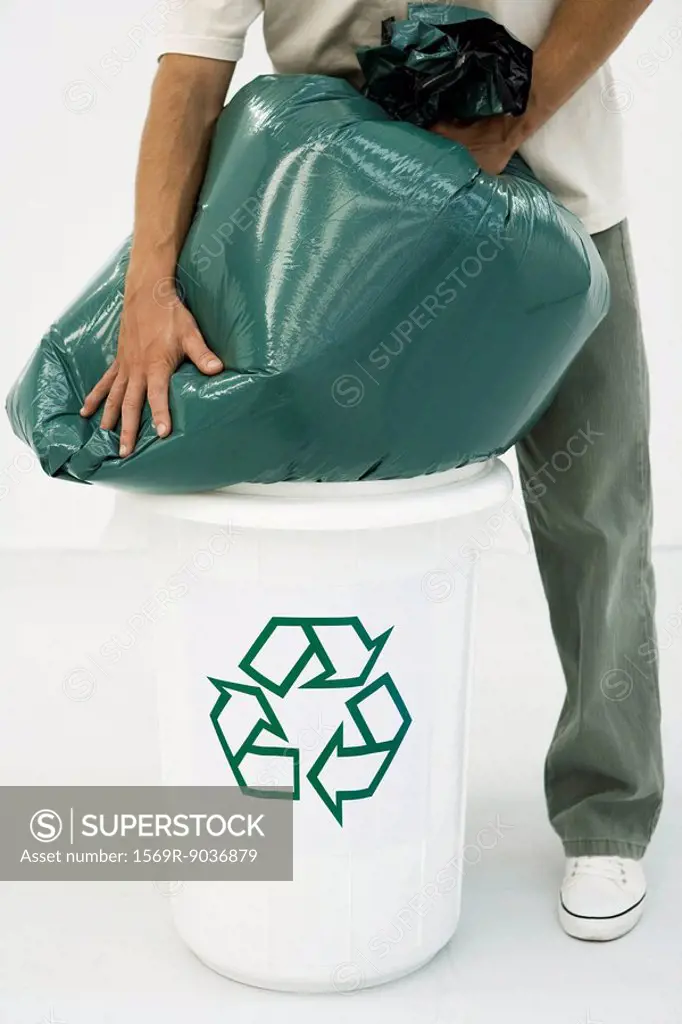 Man forcing large garbage bag into recycling bin, cropped view