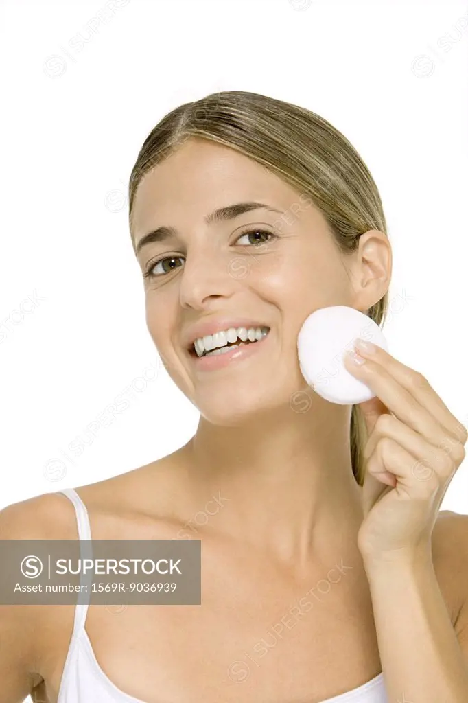 Woman wiping face with cotton cosmetic pad, smiling at camera