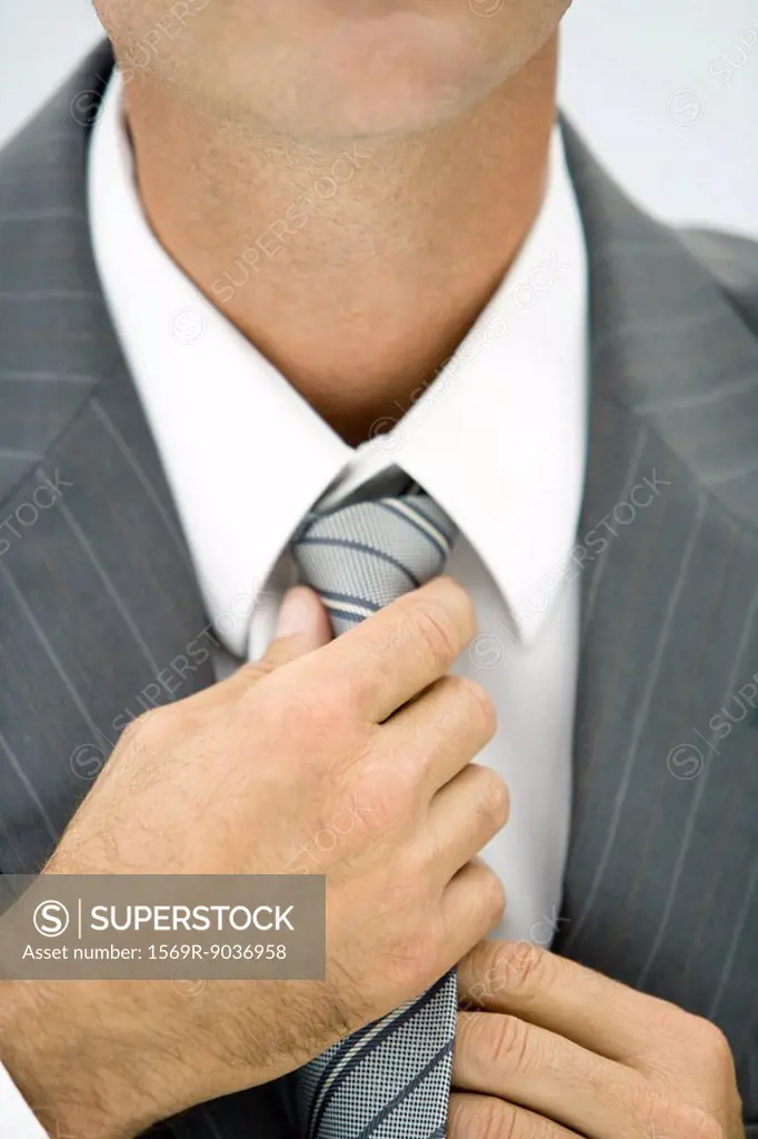 Businessman adjusting neck tie, close-up, cropped