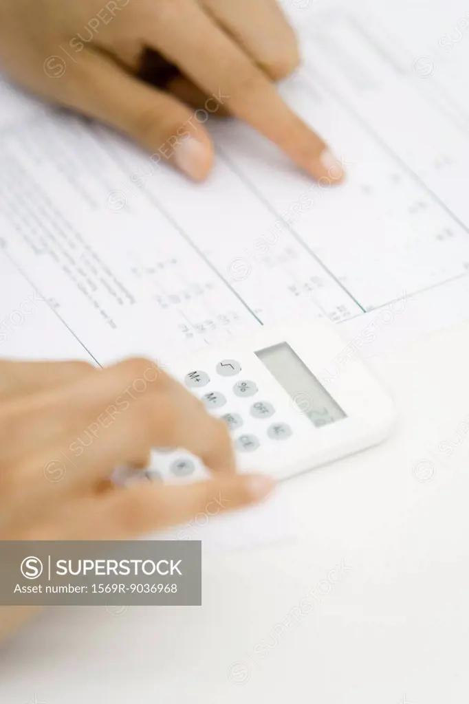 Person using calculator and pointing at document, cropped view of hands