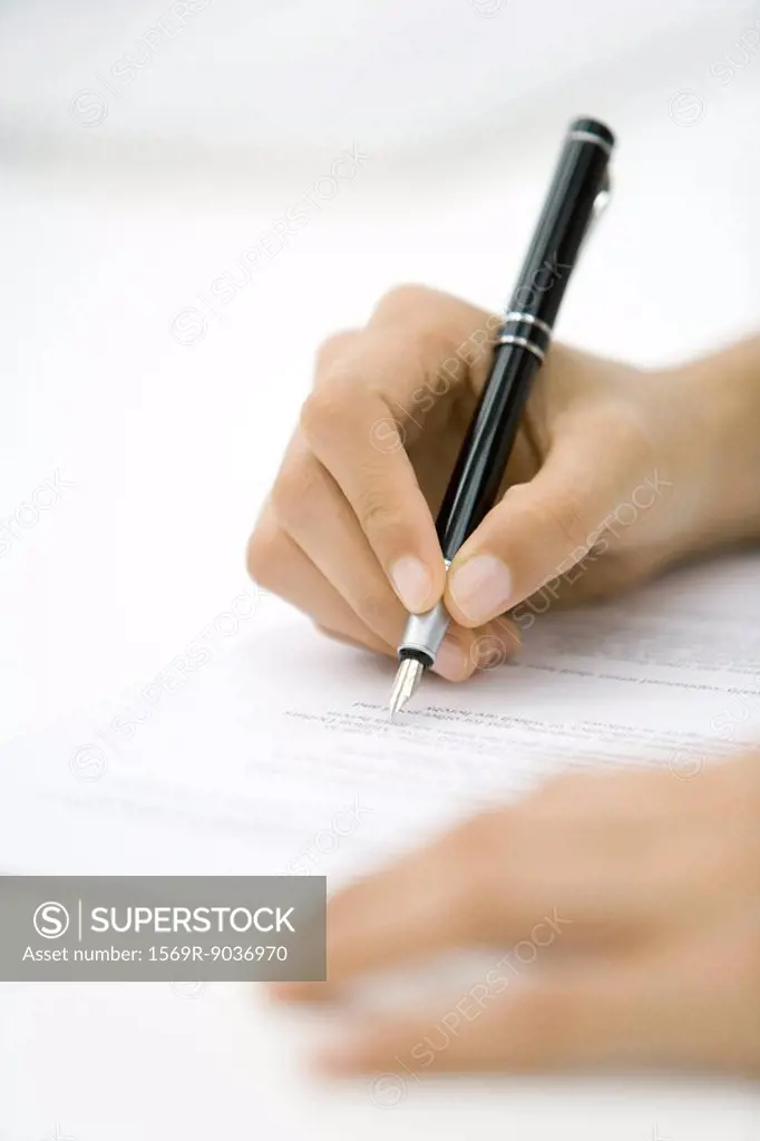 Person reviewing document, holding pen, cropped view of hands