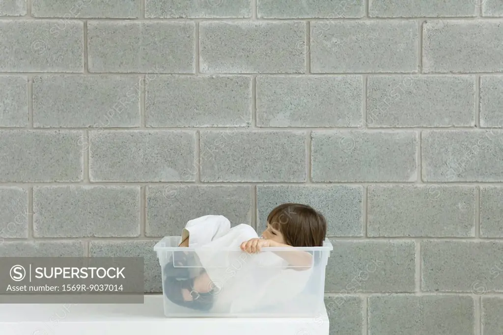 Little boy sitting inside plastic storage container, side view