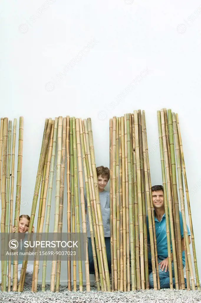 Father and two children peeking through bamboo at camera, all smiling