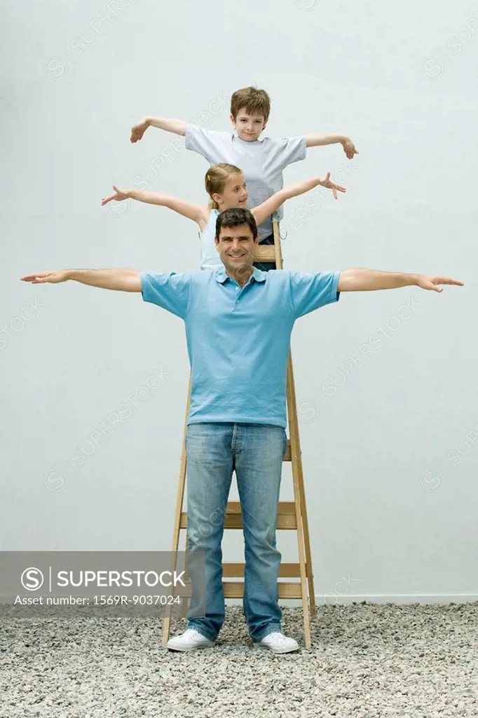 Family standing on ladder with arms out, girl looking away, father and son smiling at camera