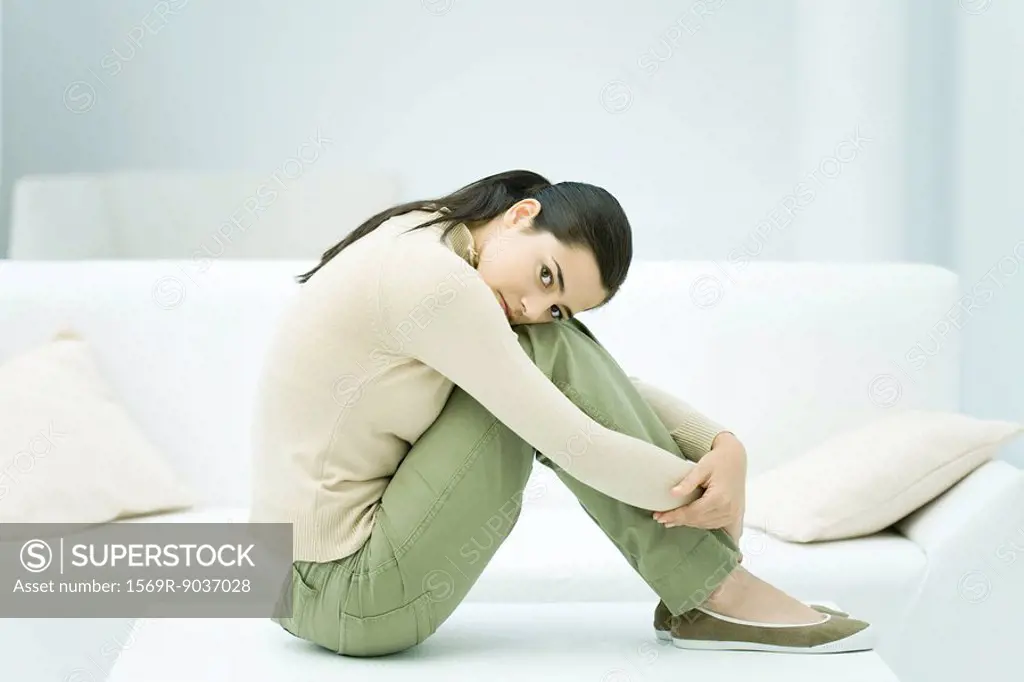 Woman sitting on coffee table, hugging knees, looking at camera