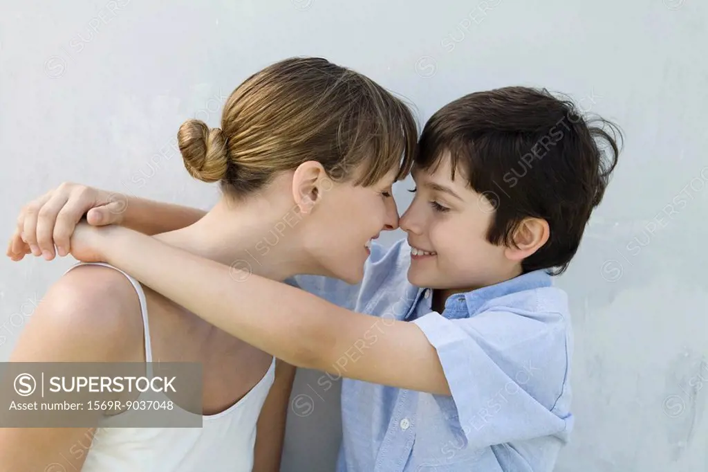 Mother and son touching noses, boy´s arms around woman, side view
