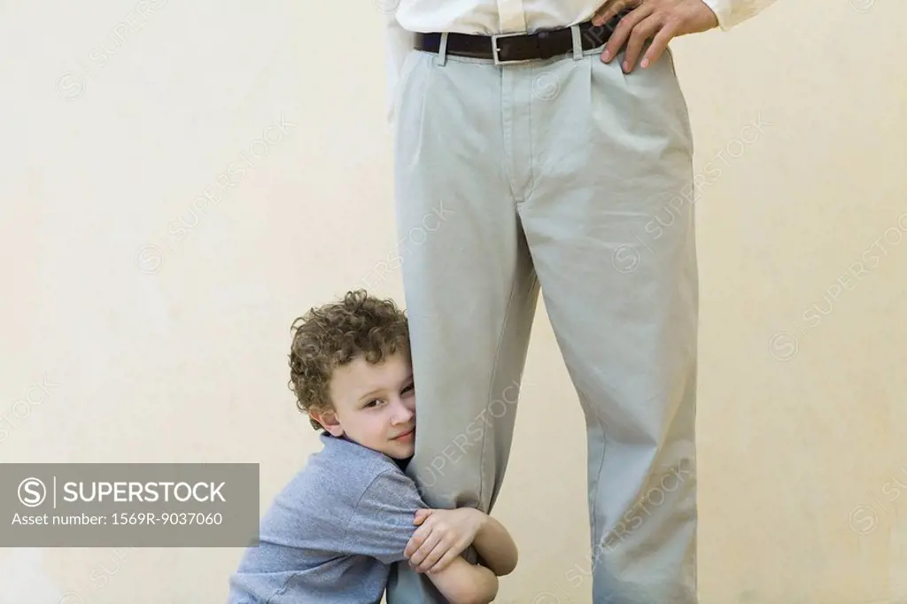 Boy clinging to his father´s leg, looking at camera, cropped view
