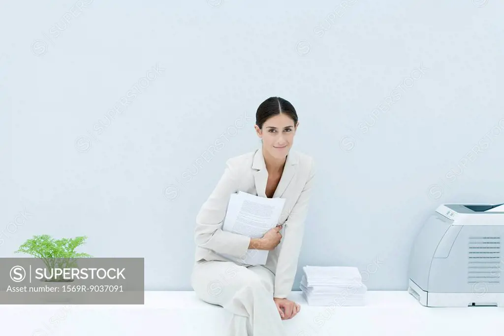 Young professional woman sitting on ledge with legs crossed, holding documents and smiling at camera