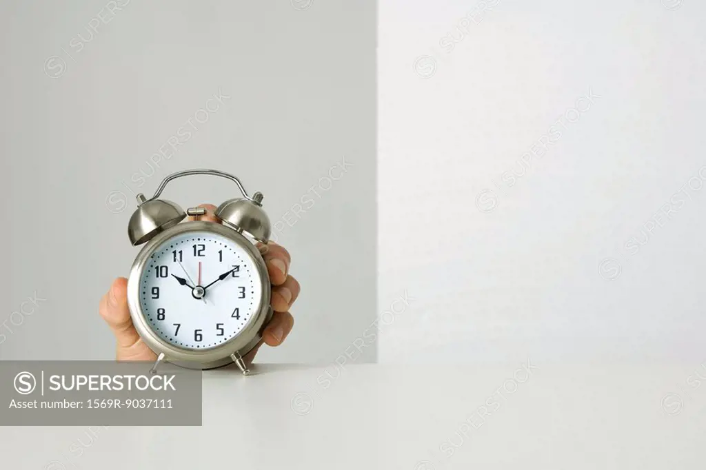 Old-fashioned alarm clock, hand reaching up to grab it from behind