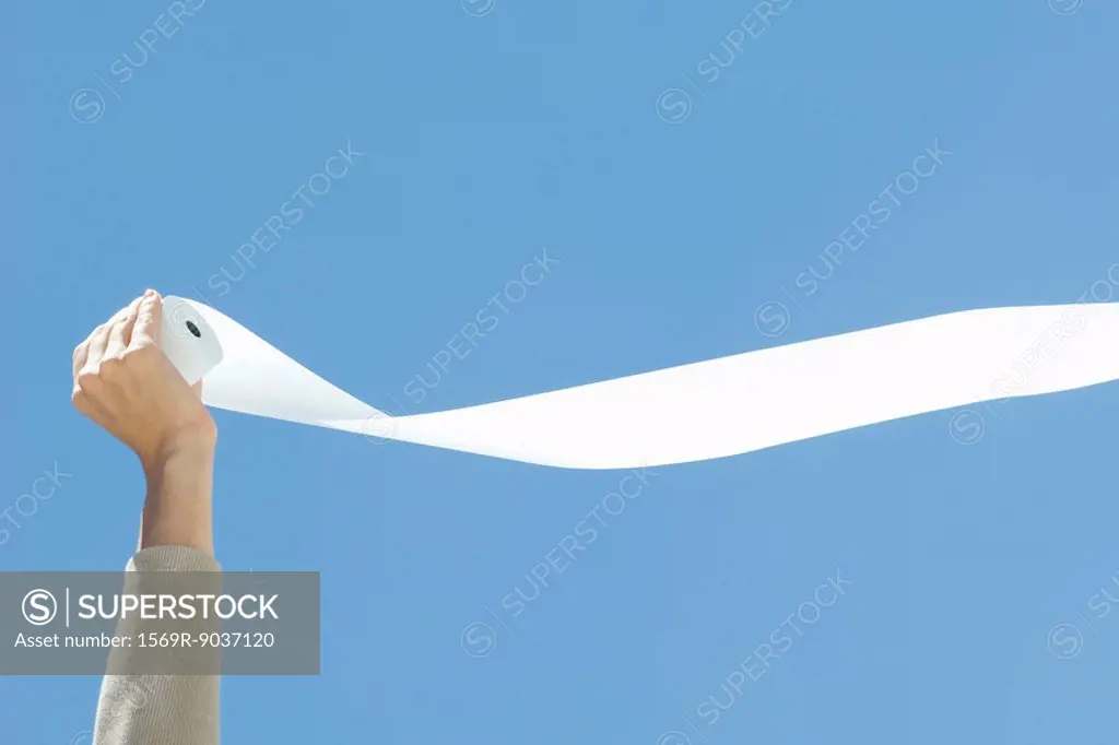 Hand holding toilet paper, unrolling in the breeze, cropped view