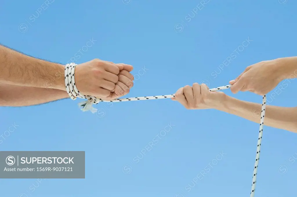 Male hands bound by rope, female hands pulling rope, cropped view