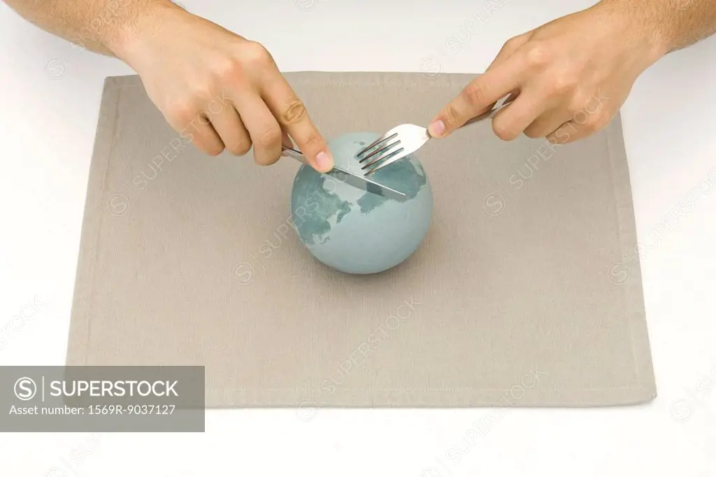 Globe resting on placemat, hands using knife and fork to cut up globe