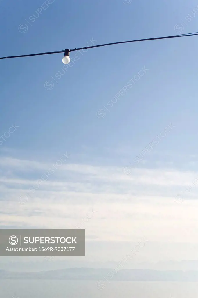 Power line with a single light bulb, cloudy sky, low angle view