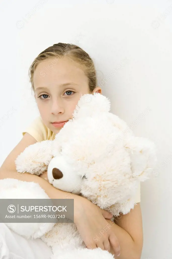 Girl holding teddy bear on her lap, looking at camera