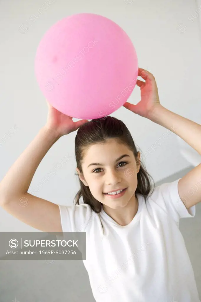 Girl holding balloon above her head, smiling at camera