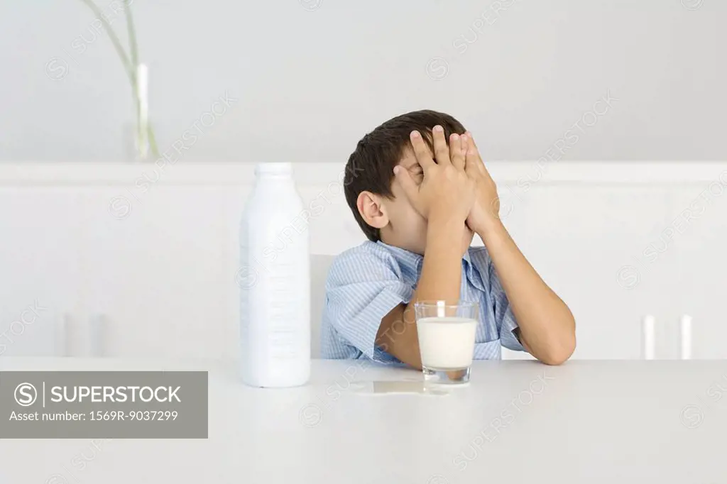 Boy with spilled milk, covering face with hands
