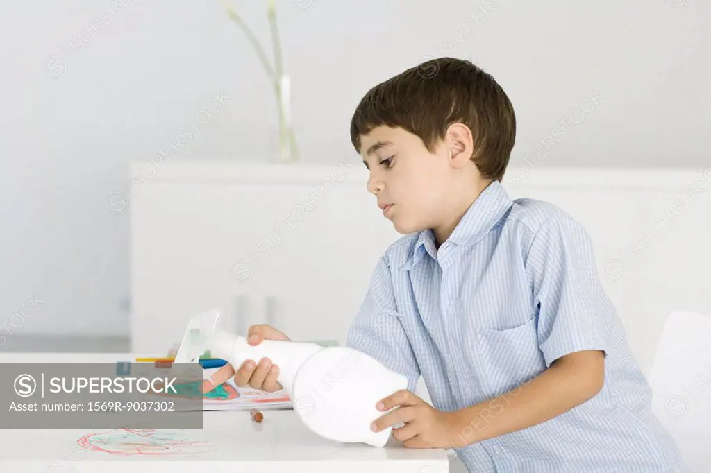 Boy cleaning crayon scribbles off of table, holding spray bottle