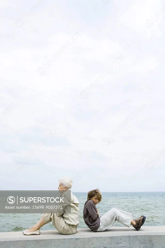 Senior woman with grandson, sitting back to back, not looking at each other