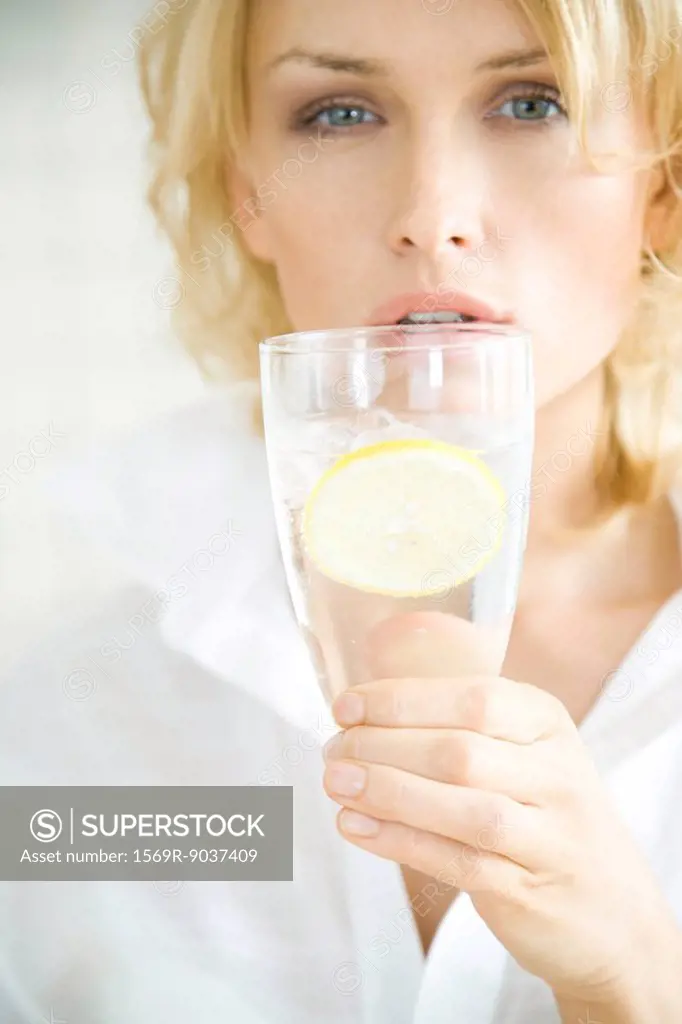 Woman holding up glass of water, looking at camera