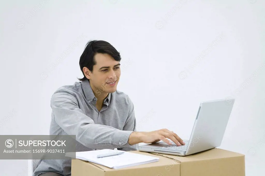 Man sitting at cardboard box desk, using laptop computer