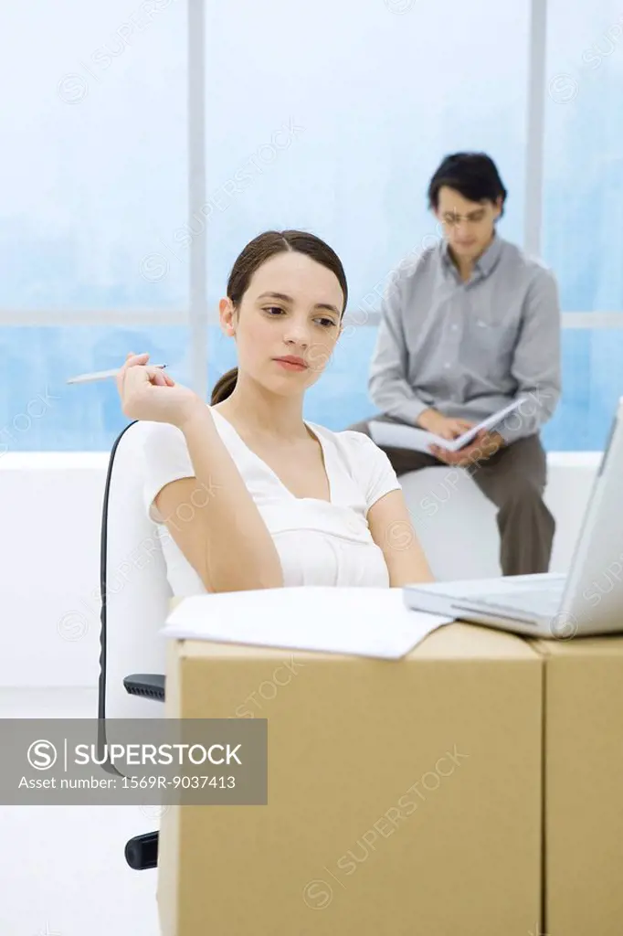 Young woman sitting at cardboard box desk, looking at laptop computer