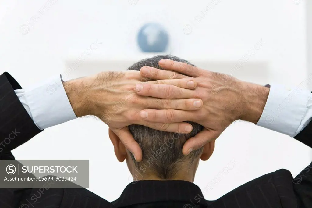 Business man with hands behind head looking at globe, rear view